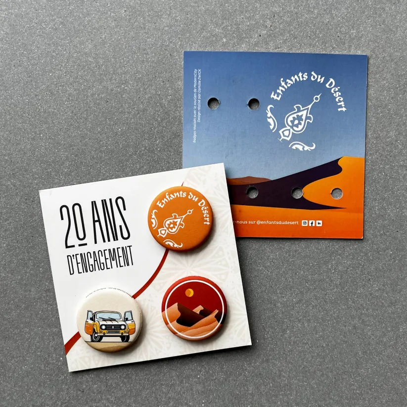 Badges Enfants du Désert posés sur leur support imprimé pour les 20 ans d’anniversaire de l’association.